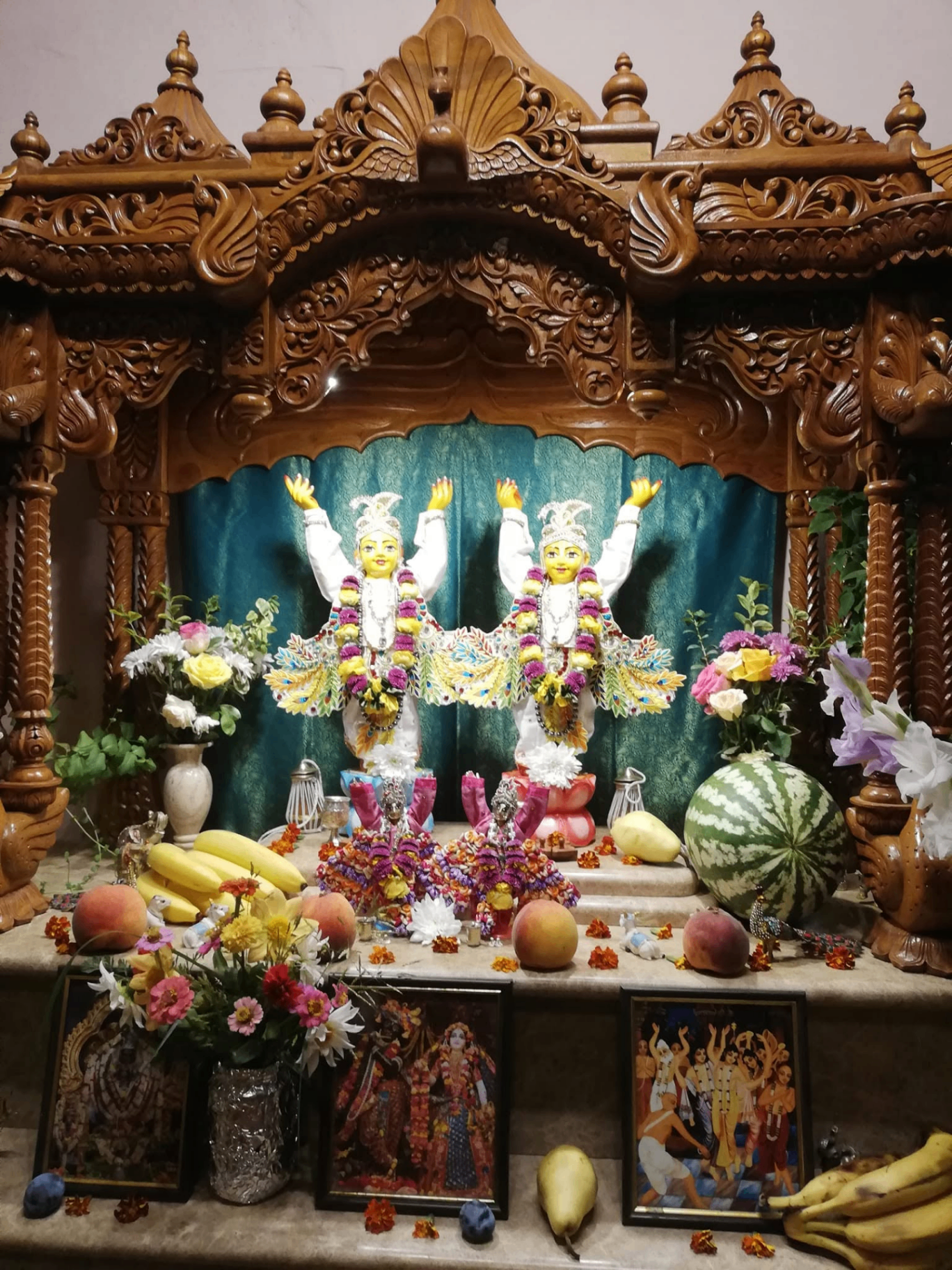 Śrī Śrī Gaura-Nitāi on the hand-carved altar, adorned with fruit and flowers